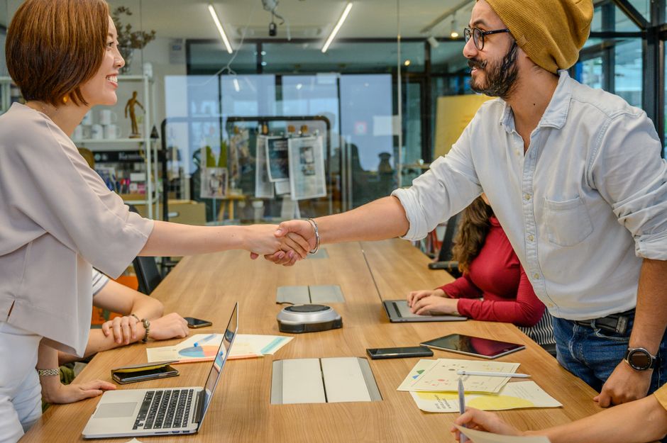 Diverse team in a modern office engaged in a collaborative meeting, sealing a partnership with a handshake.